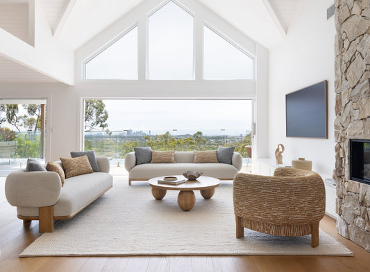 A serene coastal living room with gray and white furniture, natural textures, and a large window overlooking the ocean